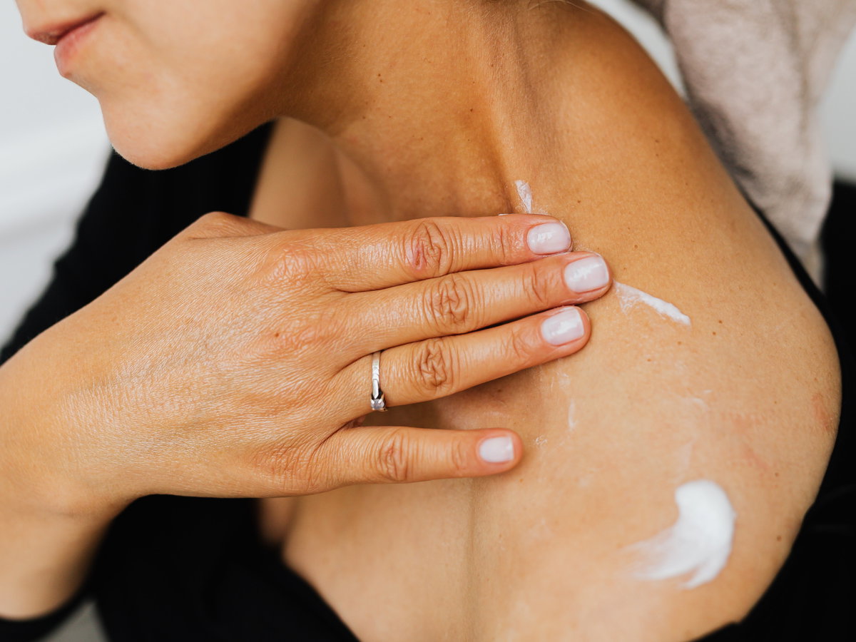 Frau trägt Bodylotion auf ihre Schulter auf.
