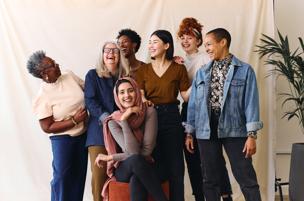 Eine Gruppe Frauen steht vor einem weißen Hintergrund und lacht