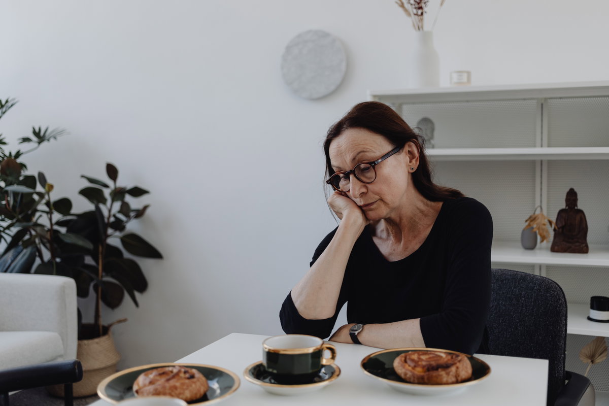 Ältere Frau sitzt traurig am Esstisch