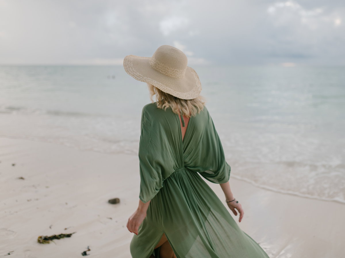 Frau mit grünem Kleid und Strohhut am Strand