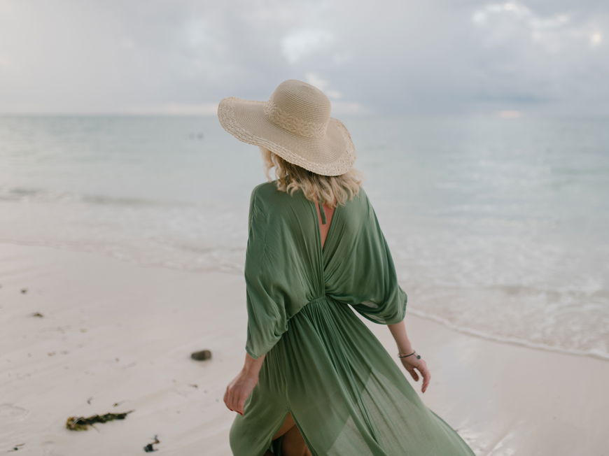 Frau mit grünem Kleid und Strohhut am Strand