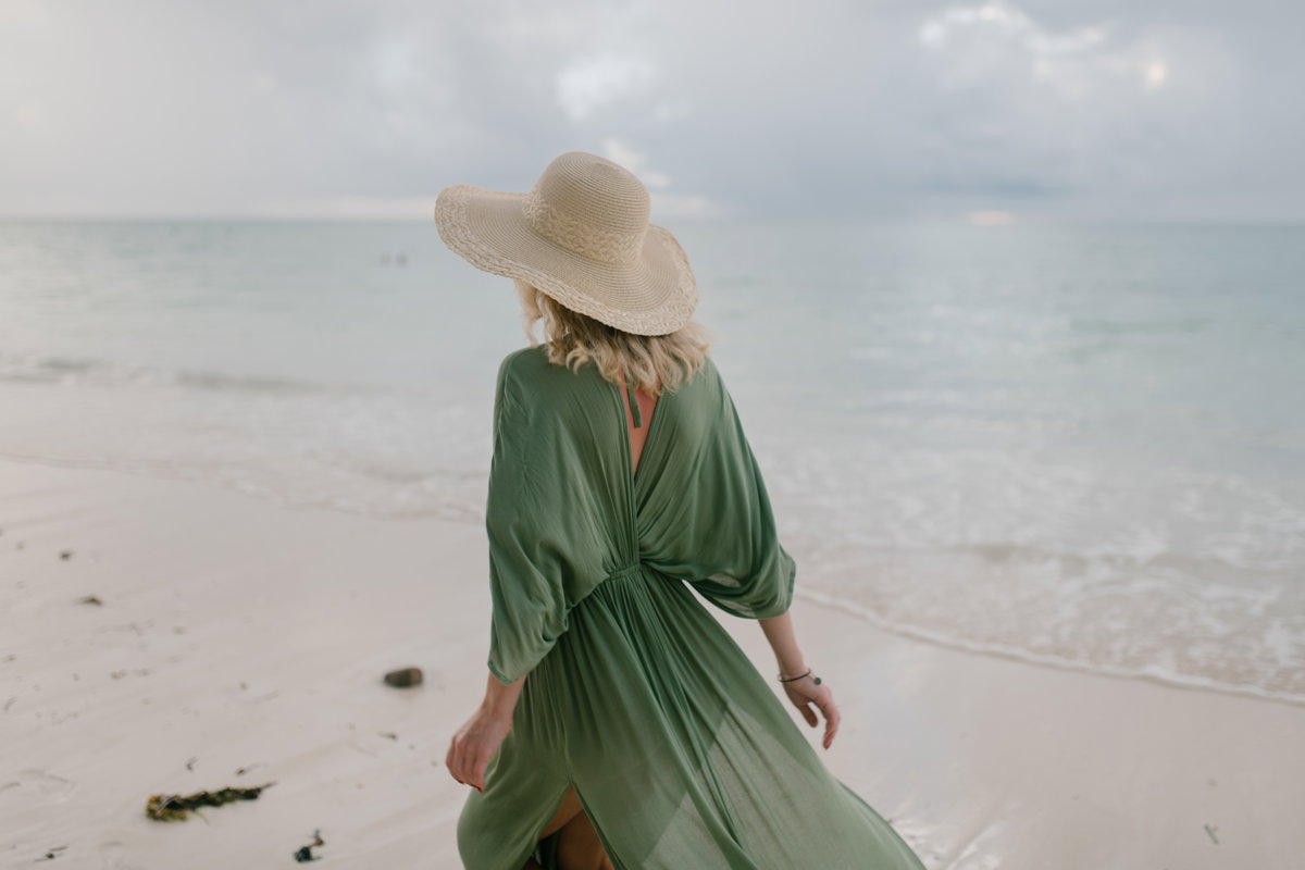 Frau mit grünem Kleid und Strohhut am Strand