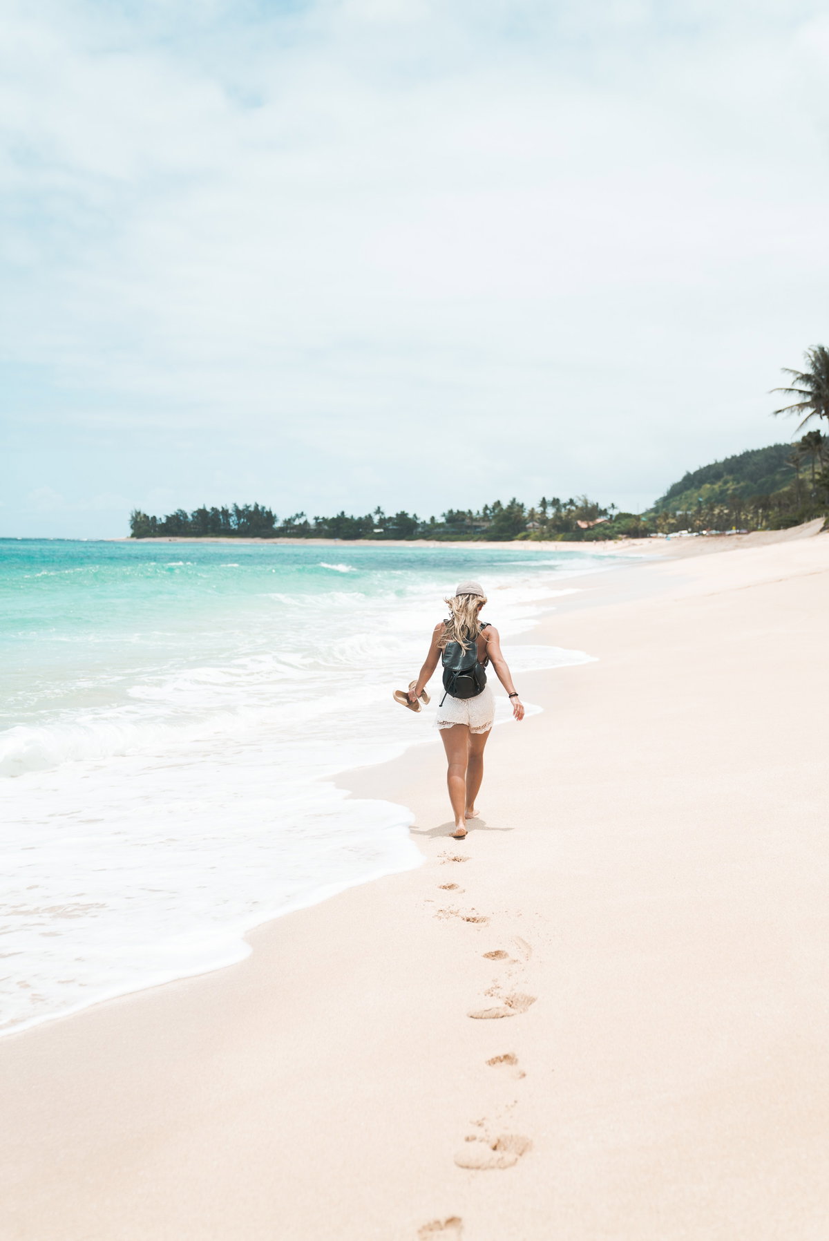 Frau mit weißen Shorts und Hut läuft am Strand