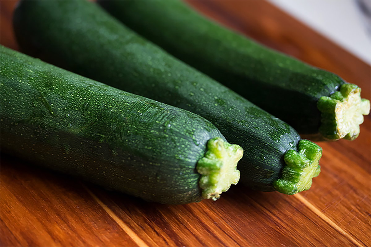Drei Zucchini liegen nebeneinander auf einem Holztisch