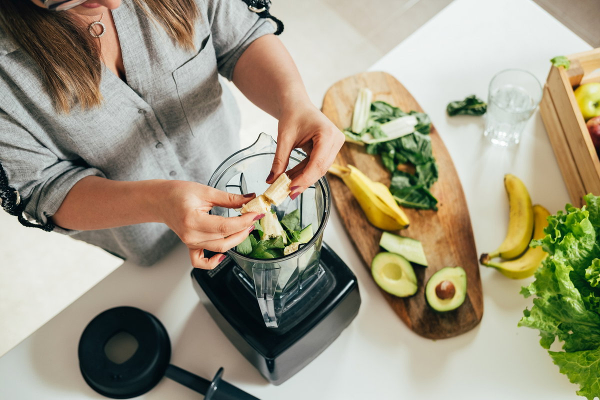 Frau legt Zutaten in einen Mixer