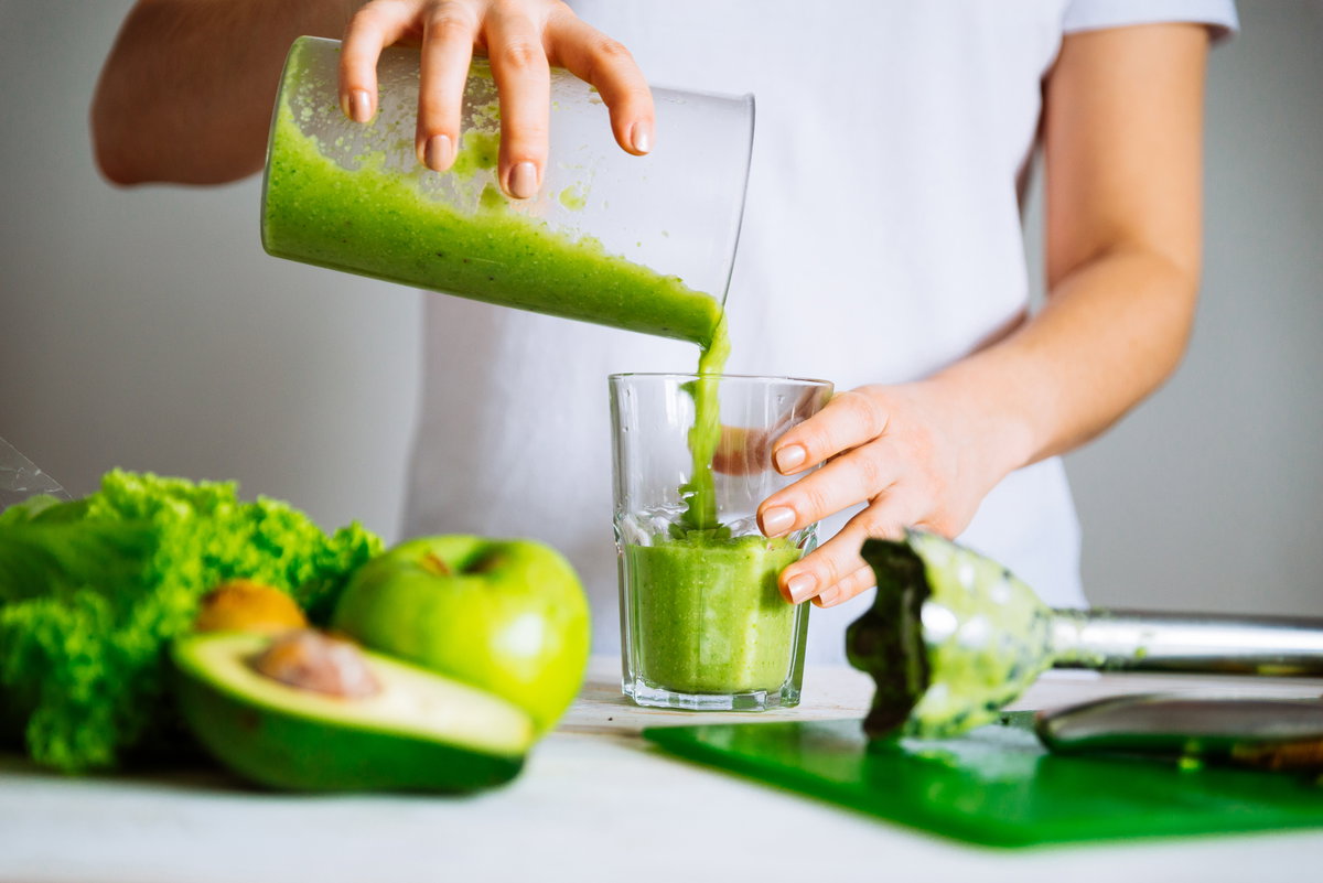 Frau im weißen T-Shirt bereitet einen grünen Smoothie vor