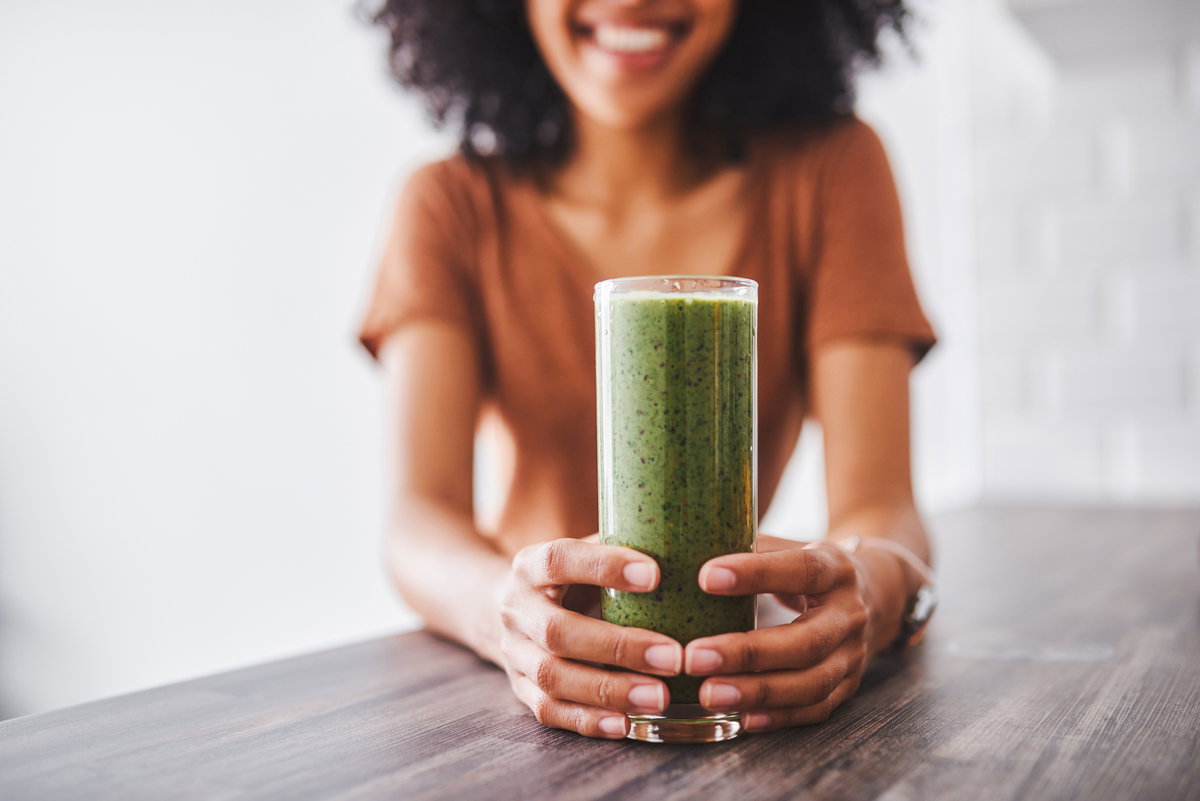 Frau hält einen Glas mit einem grünen Smoothie in der Hand