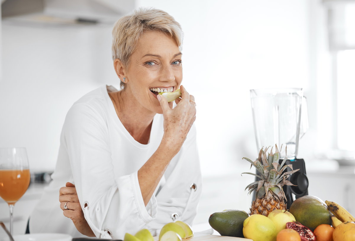 Frau mittleren Alters isst ein Stück Obst in der Küche