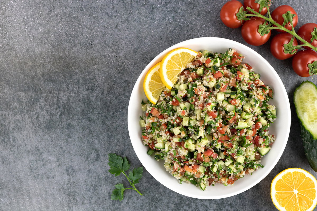 Teller mit Quinoa-Salat, Gurke, Tomaten und Zitrone steht auf einem Tisch
