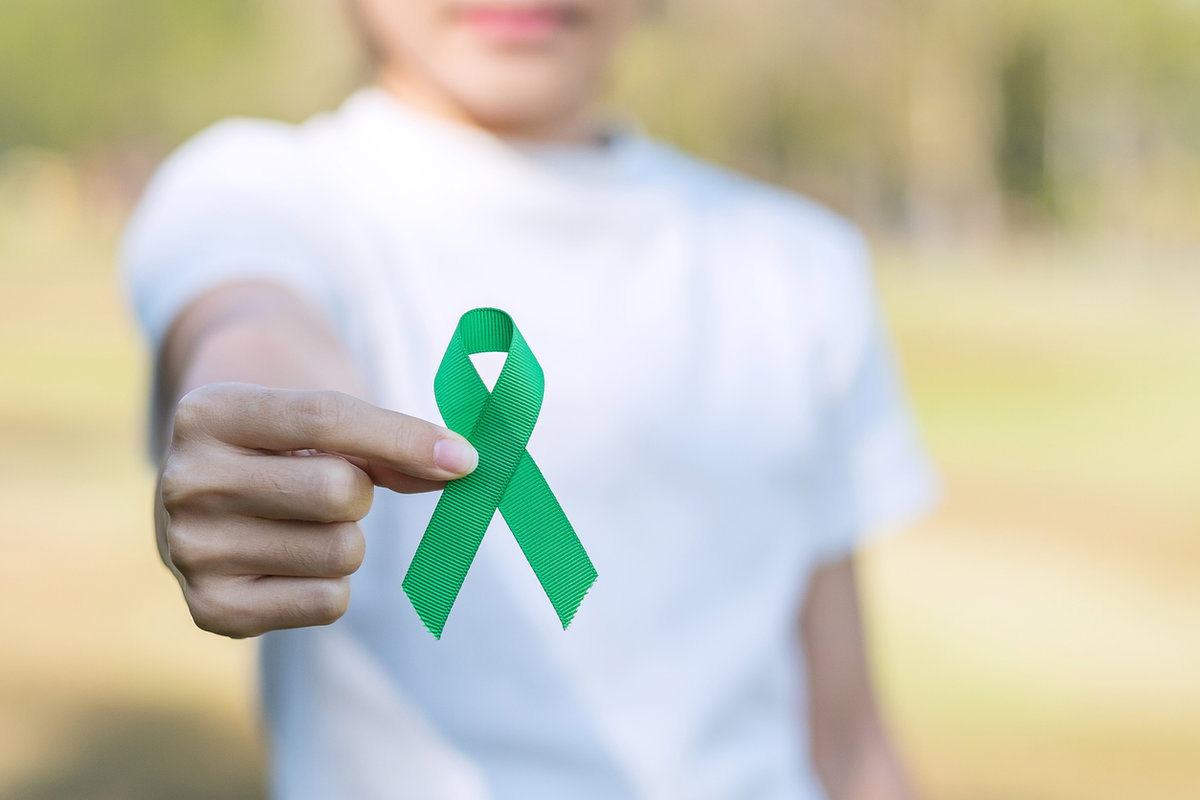 Frau im weißen T-Shirt hält eine grüne Schleife in die Kamera