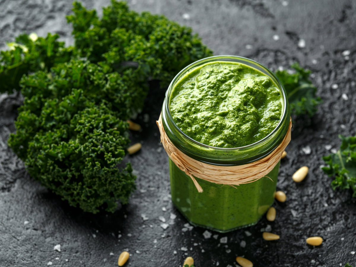 Ein Glas Grünkohl-Pesto mit Pinienkernen steht auf einem grauen Tisch