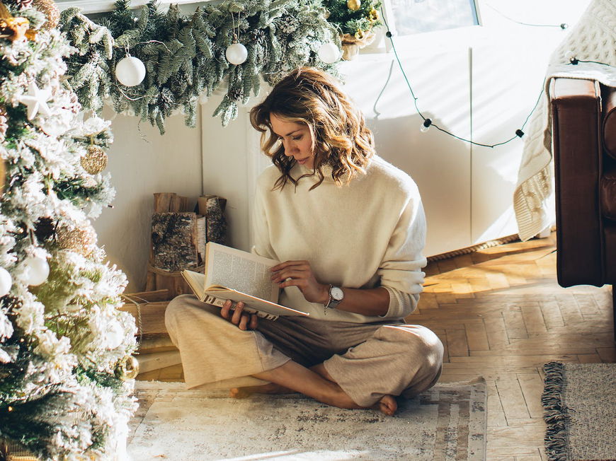 Frau liest ein Buch unter dem Weihnachtsbaum.