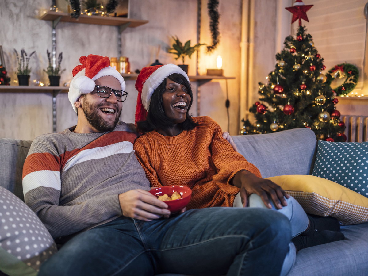 Glückliches Paar sitzt auf der Couch und guckt einen Weihnachtsfilm