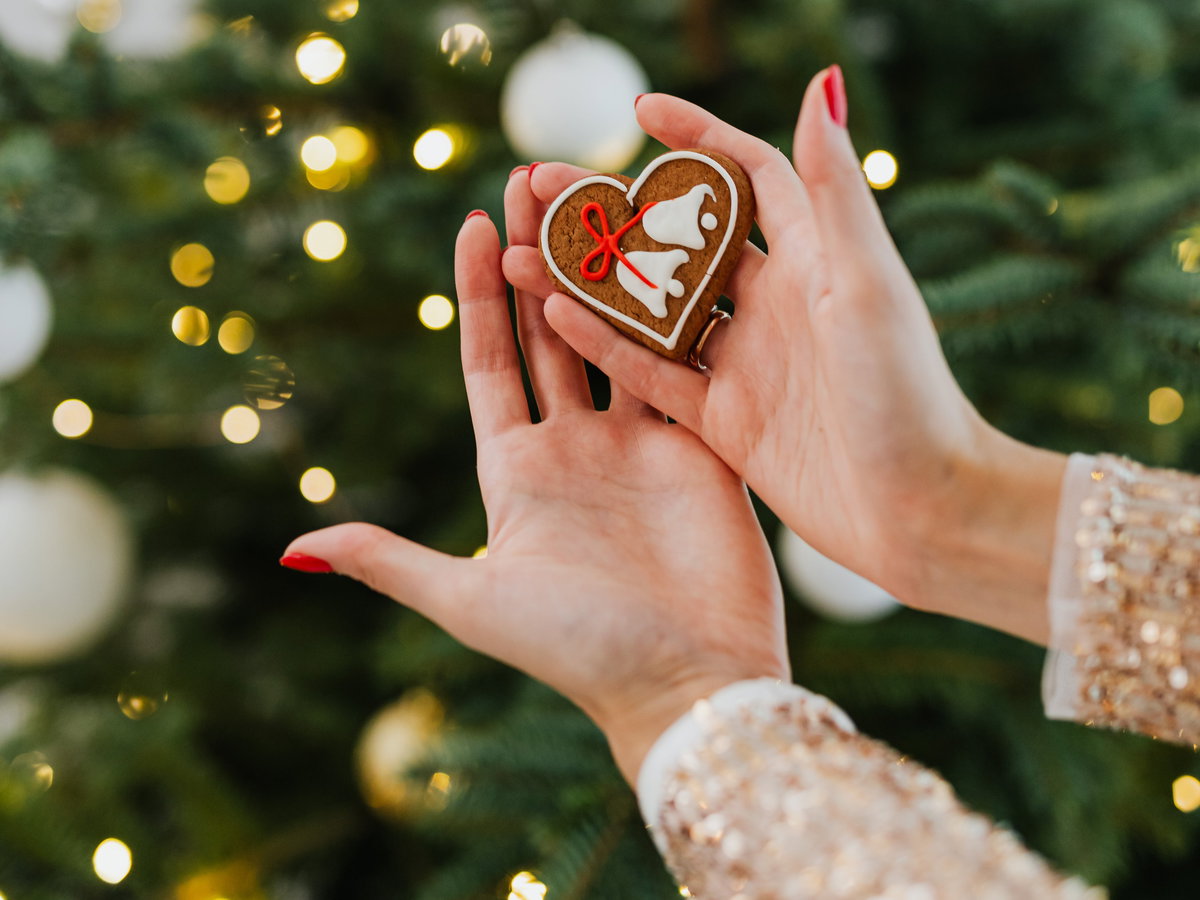 Frau hält ein Lebkuchenherz vor einem geschmückten Tannenbaum