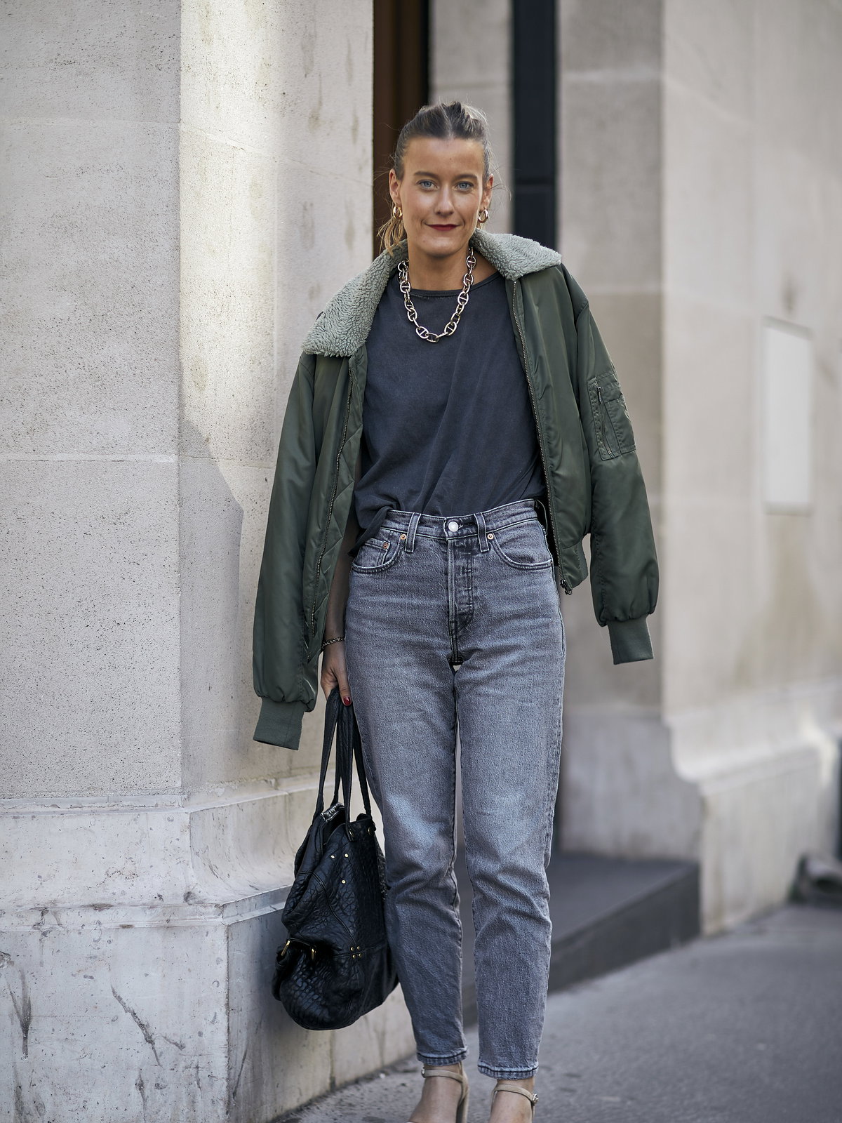 Frau trägt auf Paris Fashion Week graue Jeans, dunkelgrüne Bomberjacke, T-Shirt und Tasche