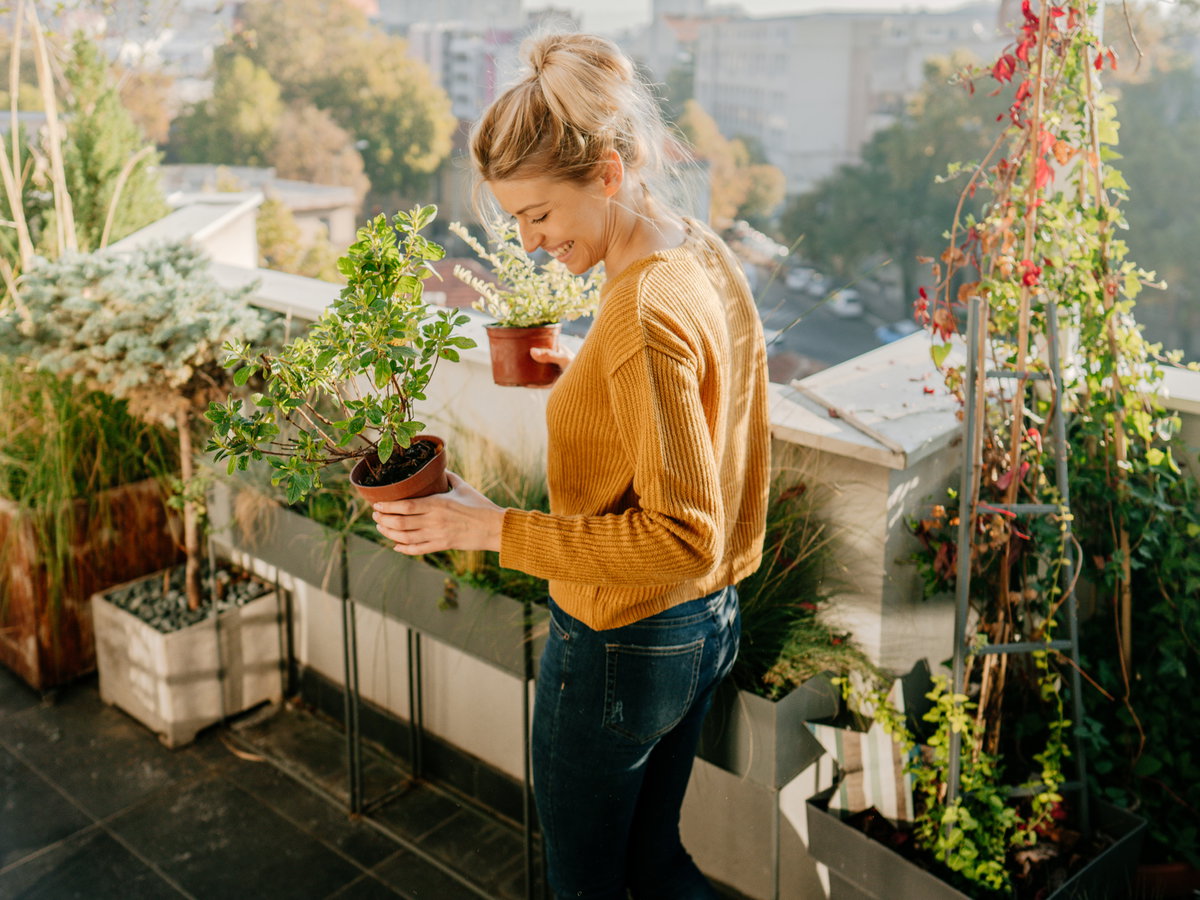 Frau steht auf einem Balkon und hält Pflanzen in der Hand