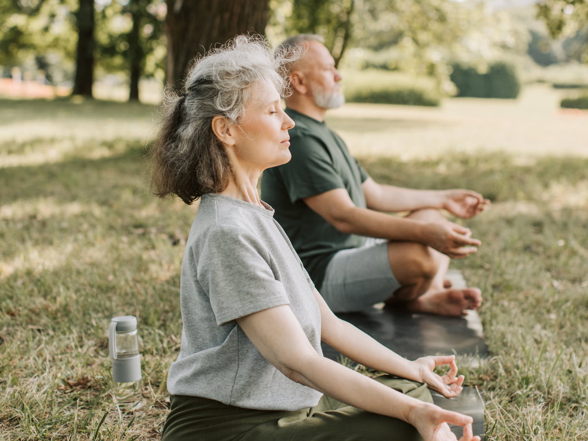 Älteres Paar macht Yoga auf einer Wiese.