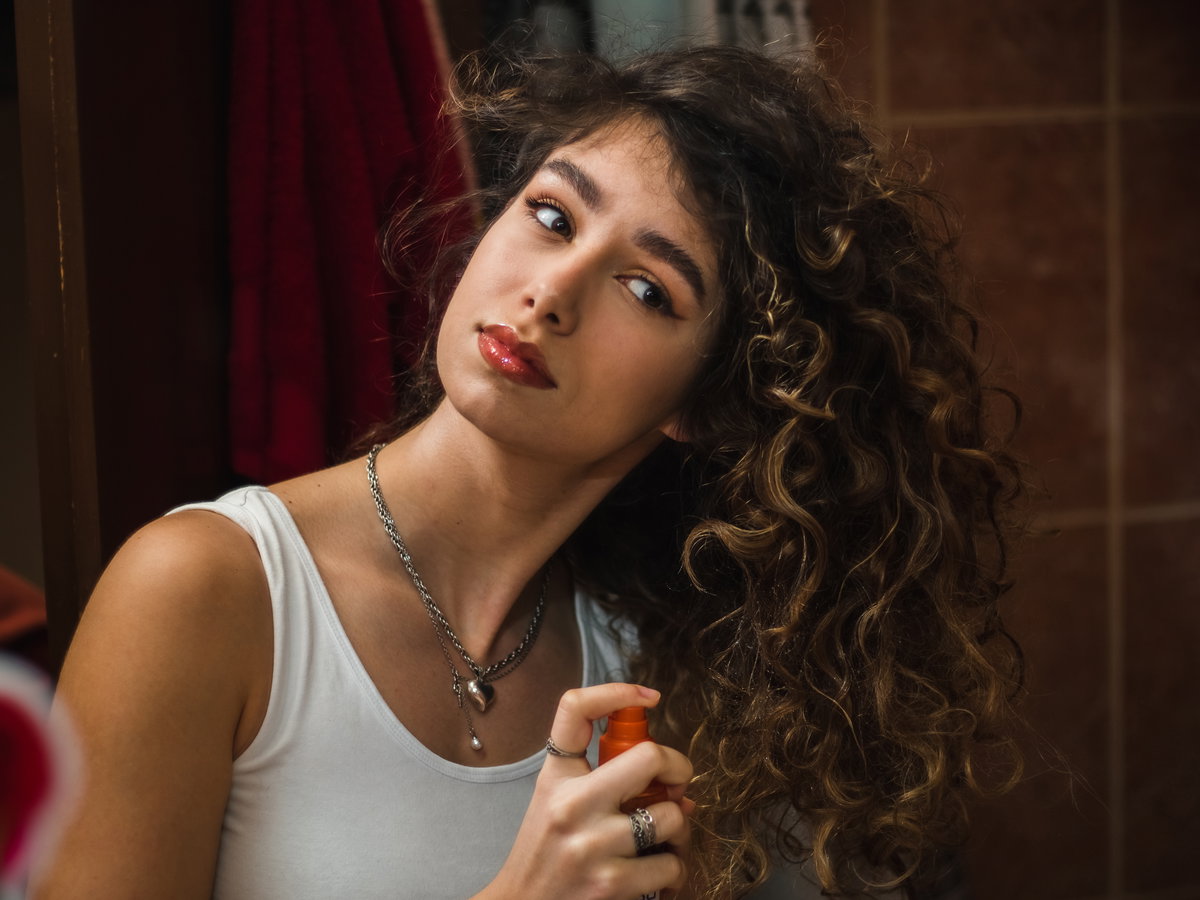 Frau mit Locken sprüht Spray in ihr Haar