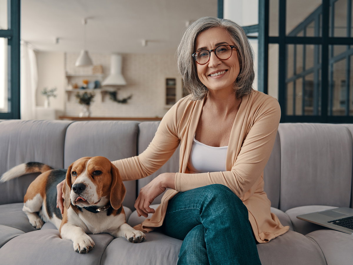 Frau mit grauen Haaren und einem Hund auf dem Sofa.