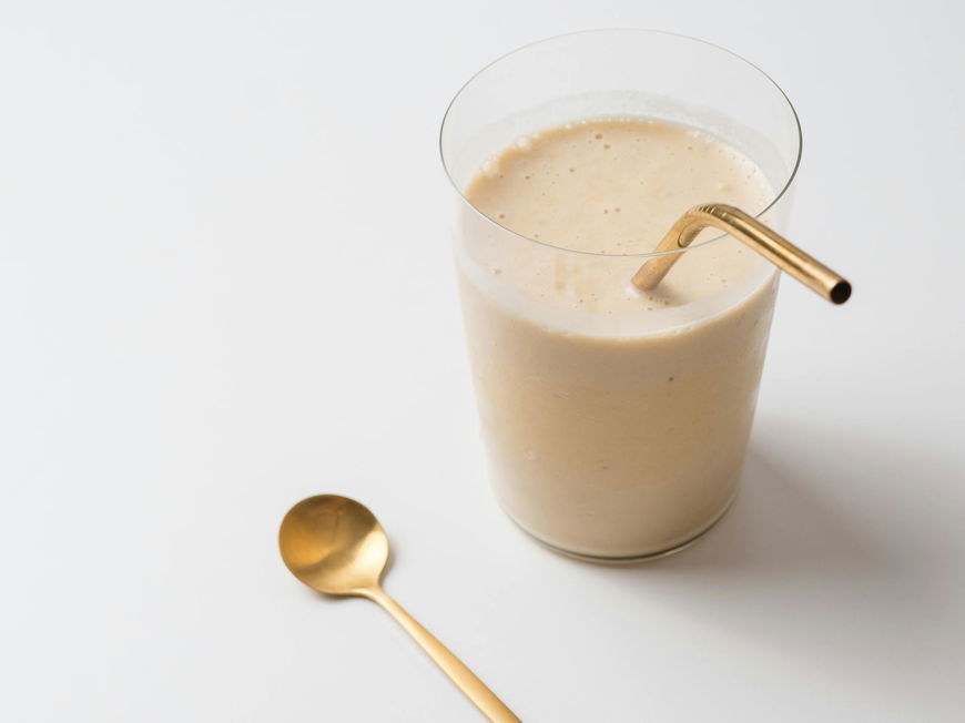 Ein cremiger Shake im Glas mit goldenem Strohhalm.