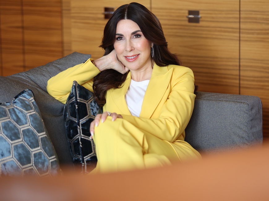 Judith Williams in gelbem Blazer auf dem Sofa.