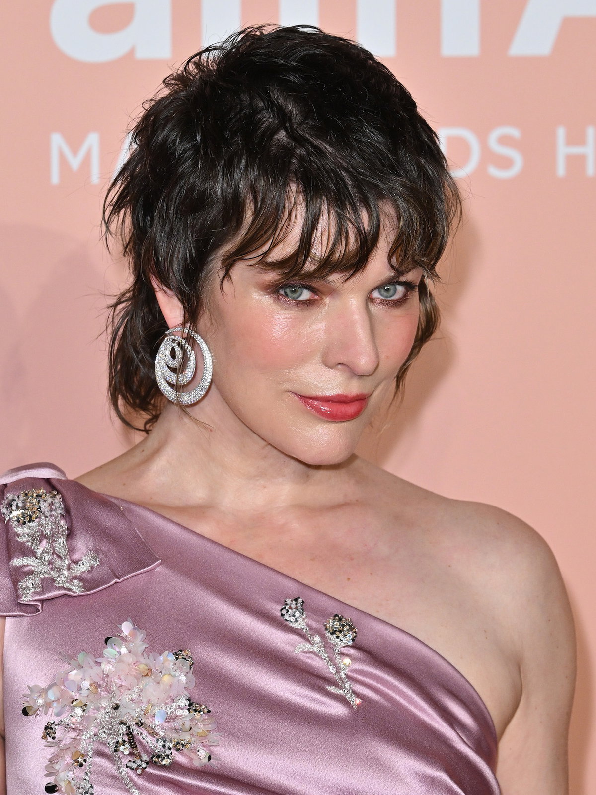 Milla Jovovich trägt rotes Rouge und roten Lippenstift.