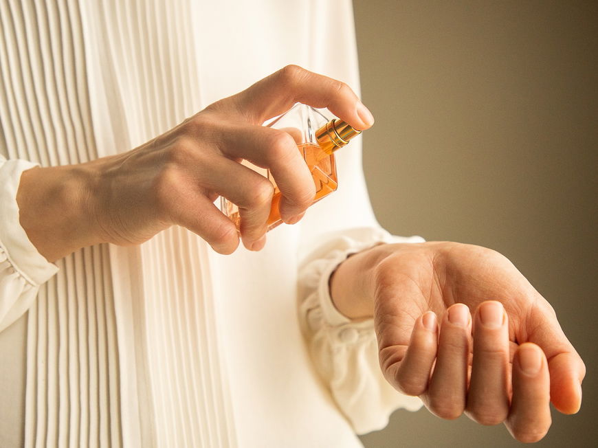 Frau mit einer weißen Bluse hält Parfum Flakon in der Hand.