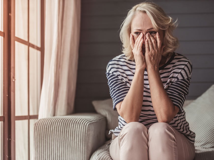 Frau sitzt auf dem Sofa und hält die Hände ins Gesicht.