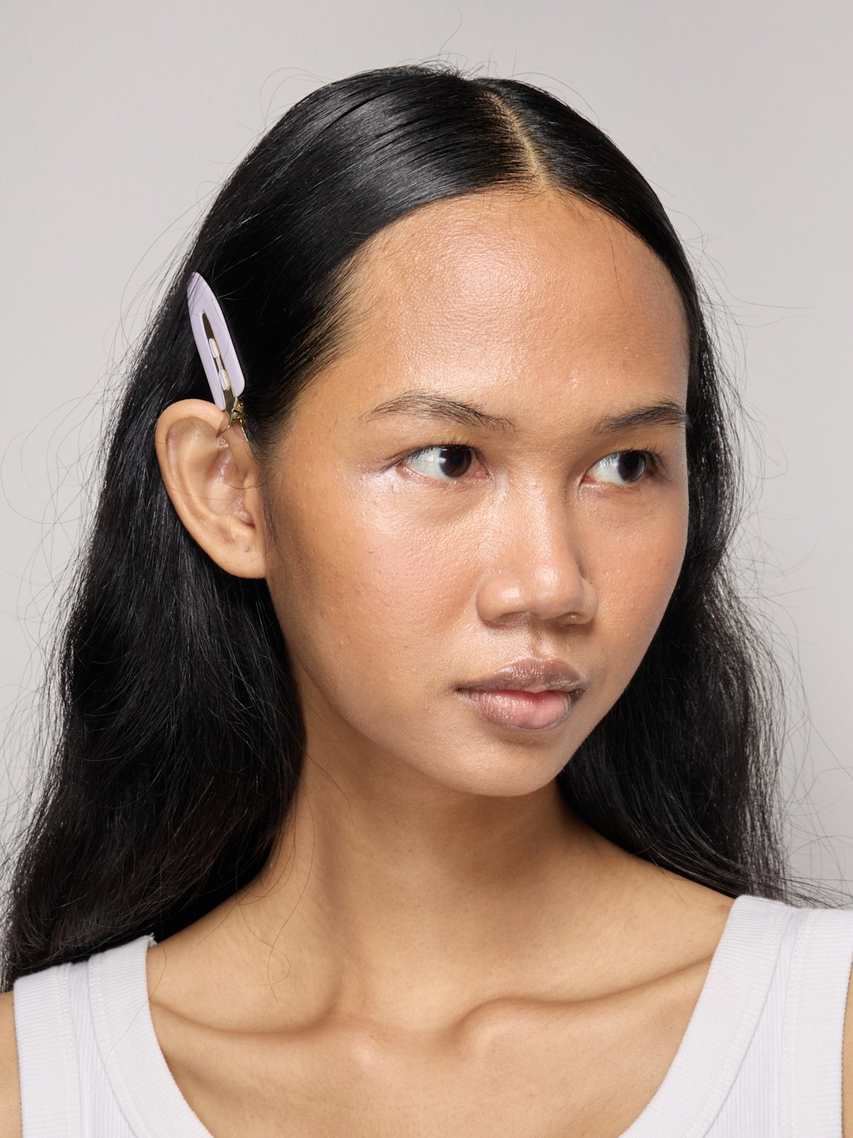 Model mit dunklen Haaren und Haarspange guckt zur Seite.