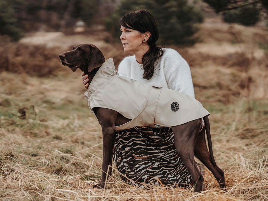 Frau hockt neben einem Hund mit Regenmantel.