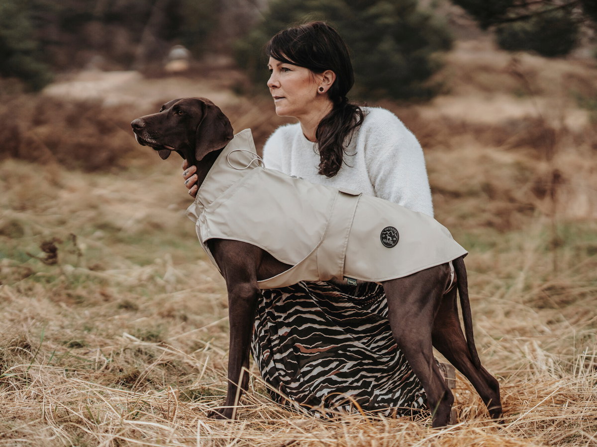 Frau hockt neben einem Hund mit Regenmantel.