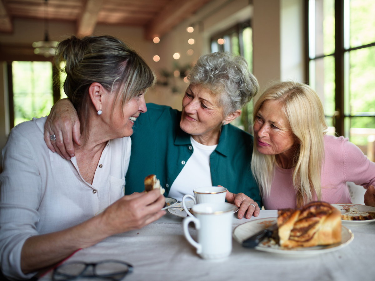 Drei Frauen sitzen am Tisch und sprechen und essen Kuchen.