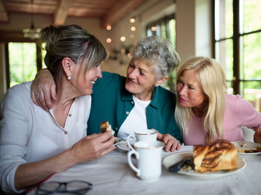 Drei Frauen sitzen am Tisch und sprechen und essen Kuchen.
