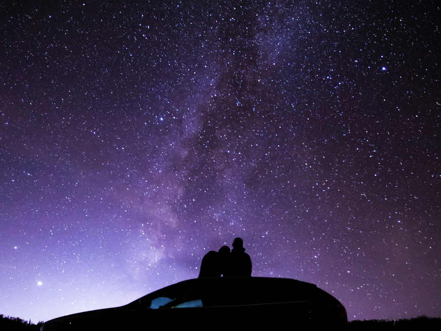 Pärchen sitzt auf Autodach und schaut in den Sternenhimmel