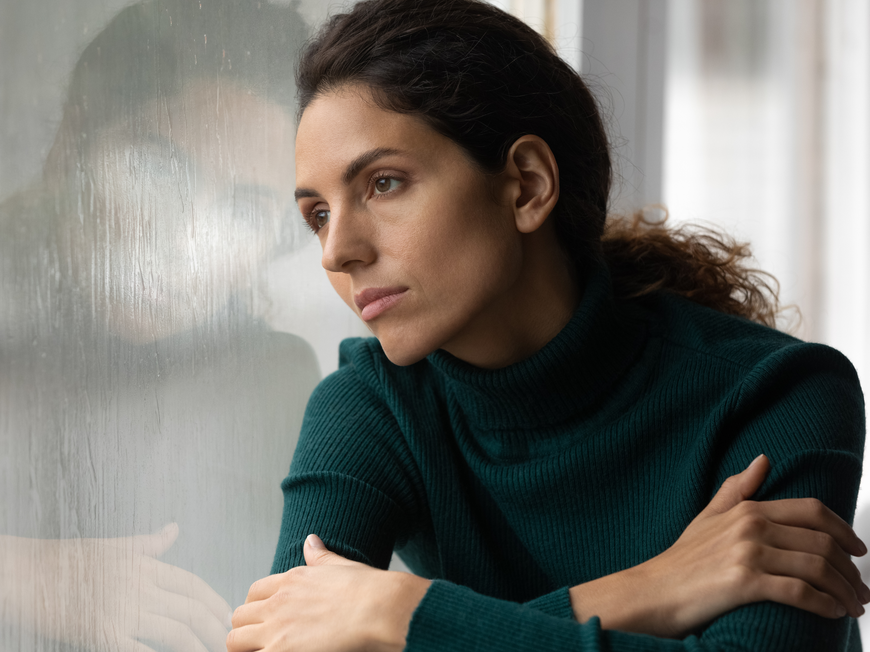Frau schaut nachdenklich aus dem Fenster
