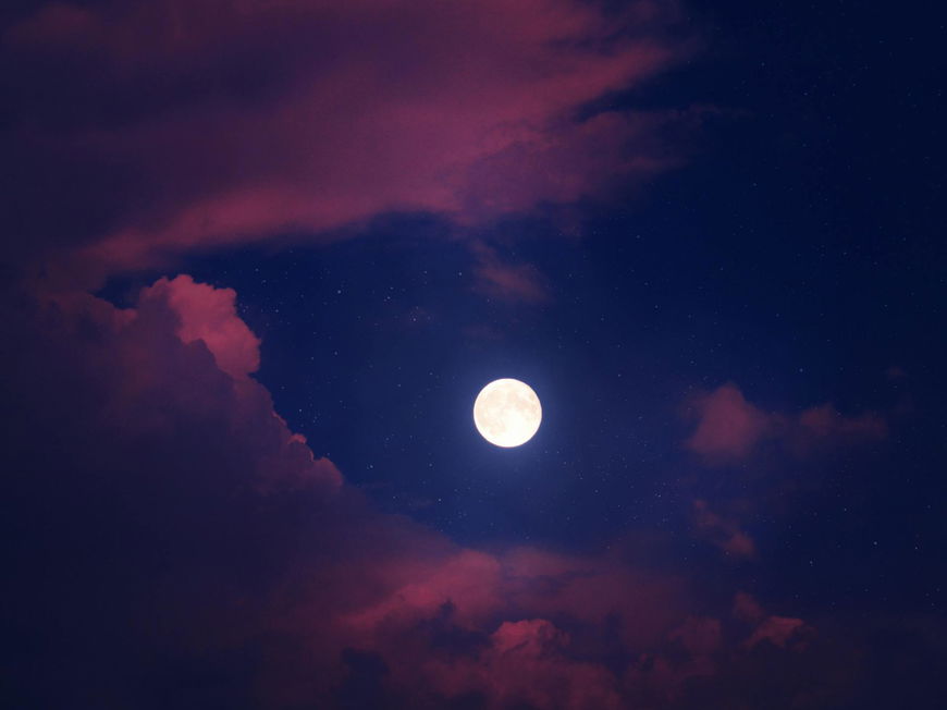 Ein Vollmond an einem blauen Himmel mit rosafarbenen Wolken.