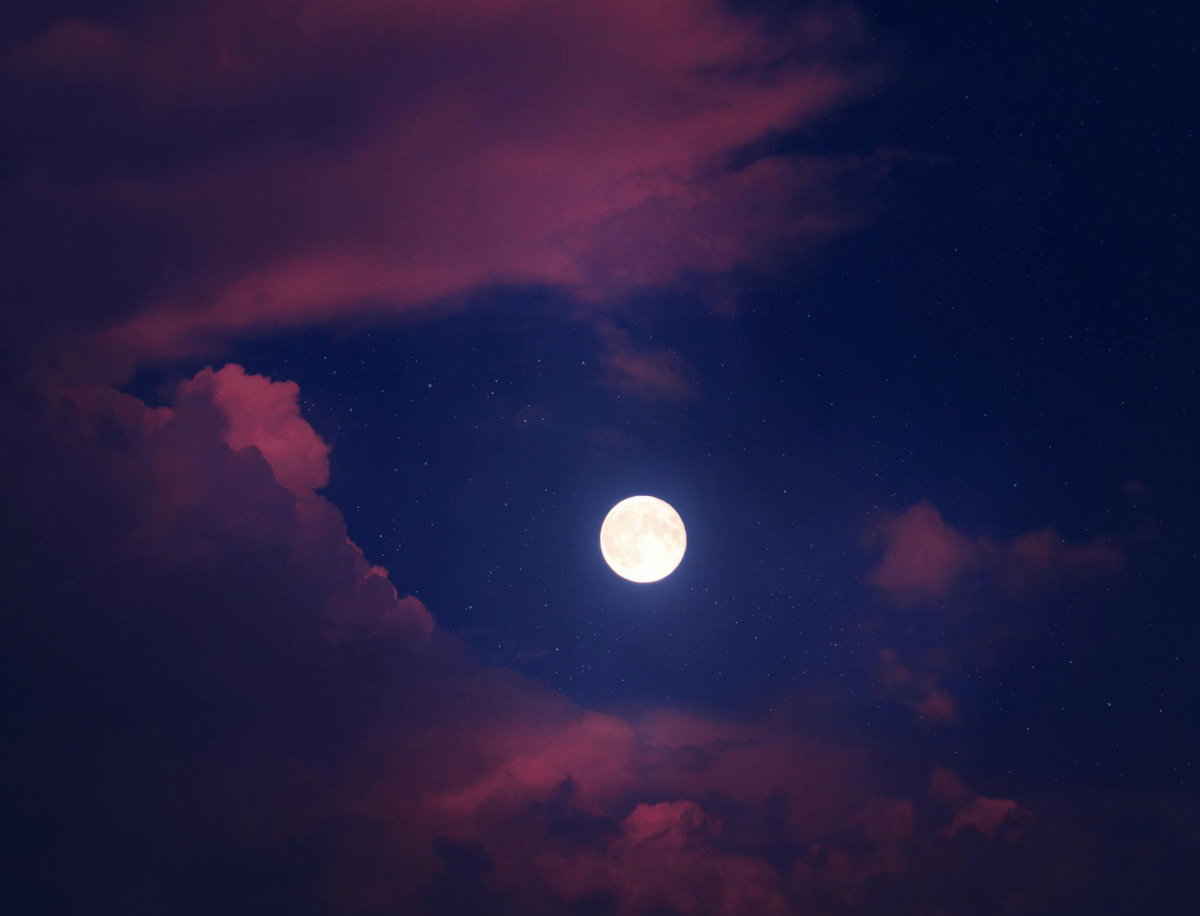 Ein Vollmond an einem blauen Himmel mit rosafarbenen Wolken.