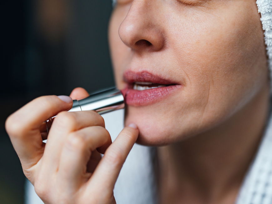 Frau trägt Lippenstift auf ihre Lippen auf.