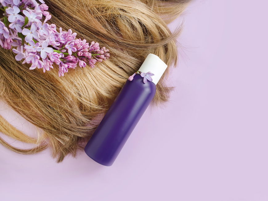 Haare einer Frau liegen mit Orchideen und einer lila Flasche auf einem rosafarbenen Hintergrund.
