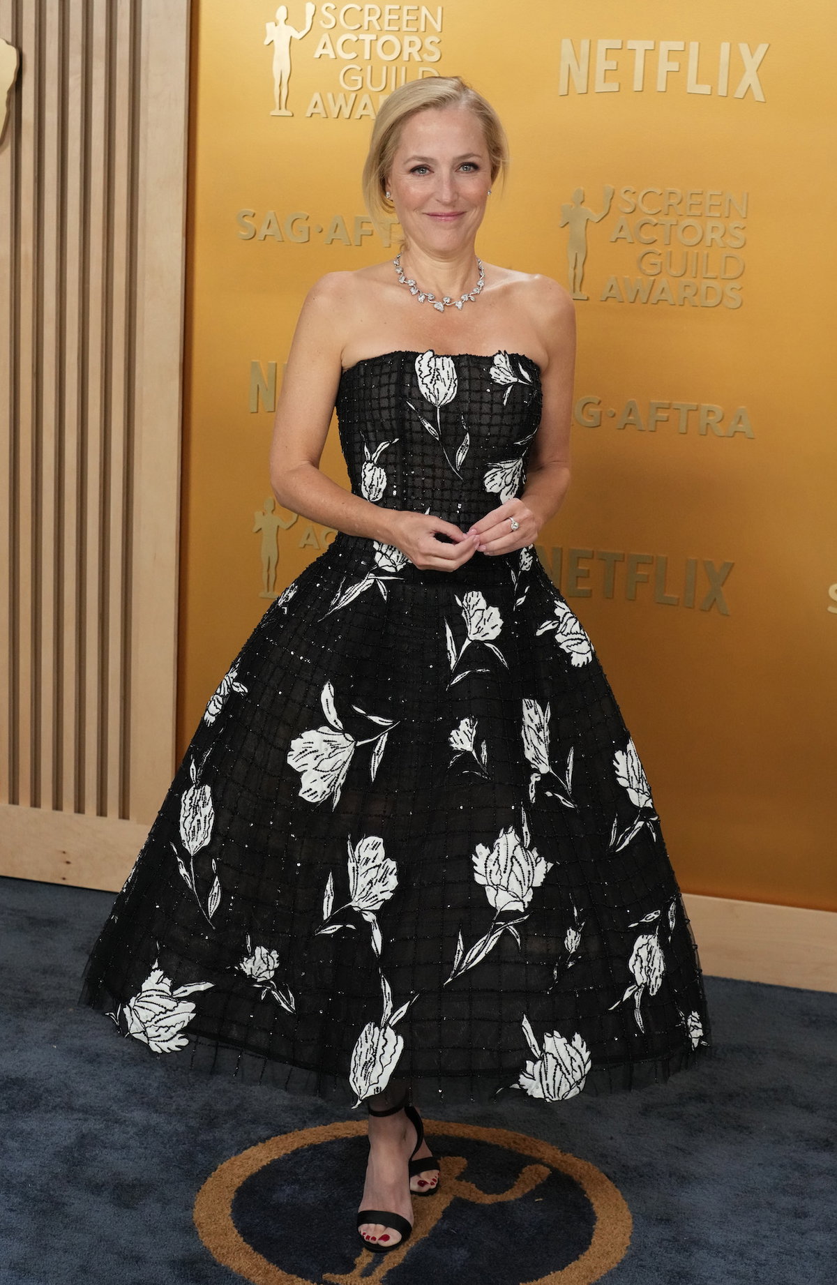 Gillian Anderson in einem schwarzen Kleid mit weißen Blumenmustern.