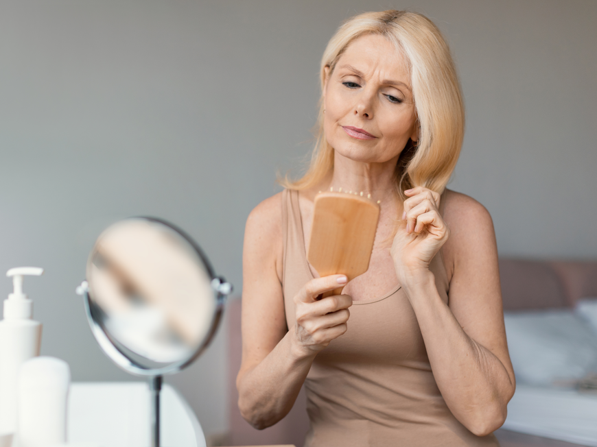 Reife Frau bürstet Haare kritisch