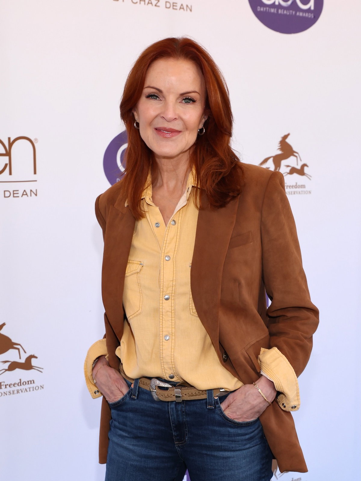 Marcia Cross mit einer Jeans, einem gelben Hemd und einem braunen Blazer auf dem roten Teppich.