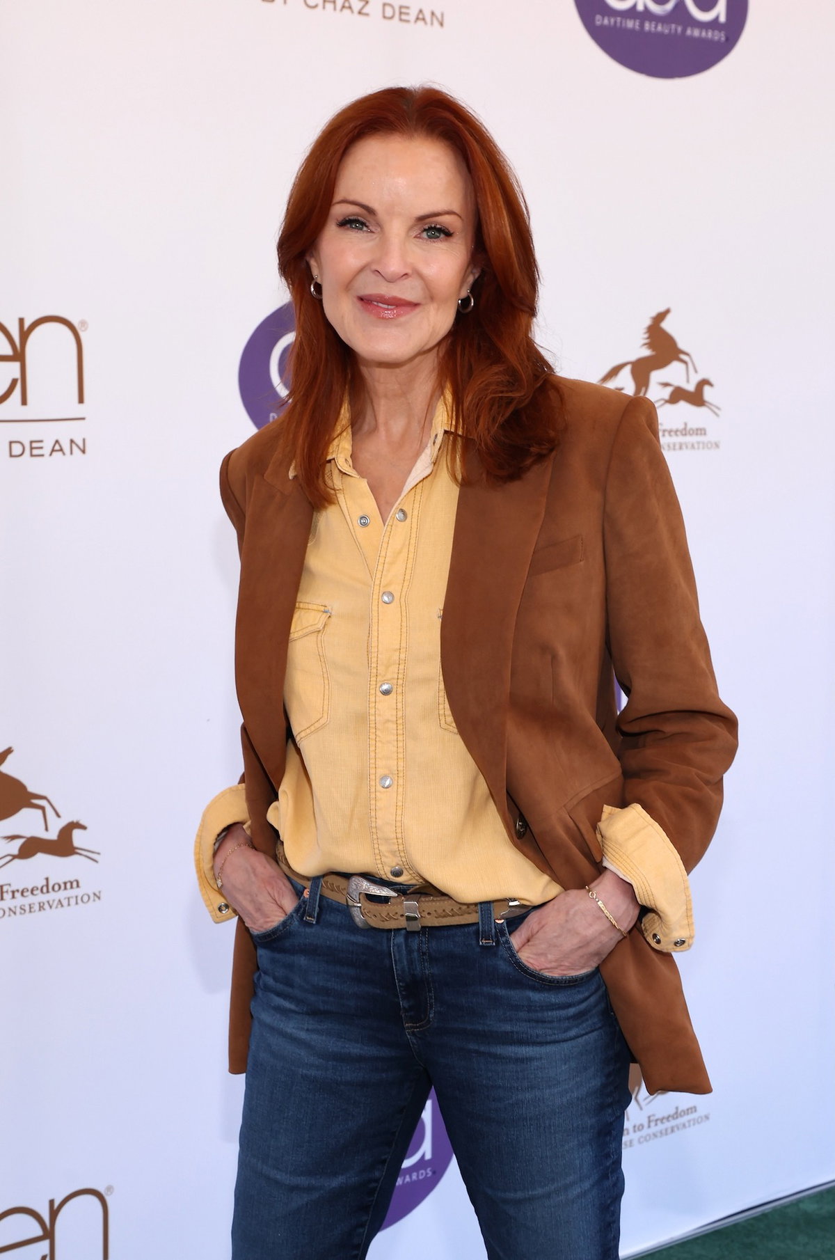 Marcia Cross mit einer Jeans, einem gelben Hemd und einem braunen Blazer auf dem roten Teppich.