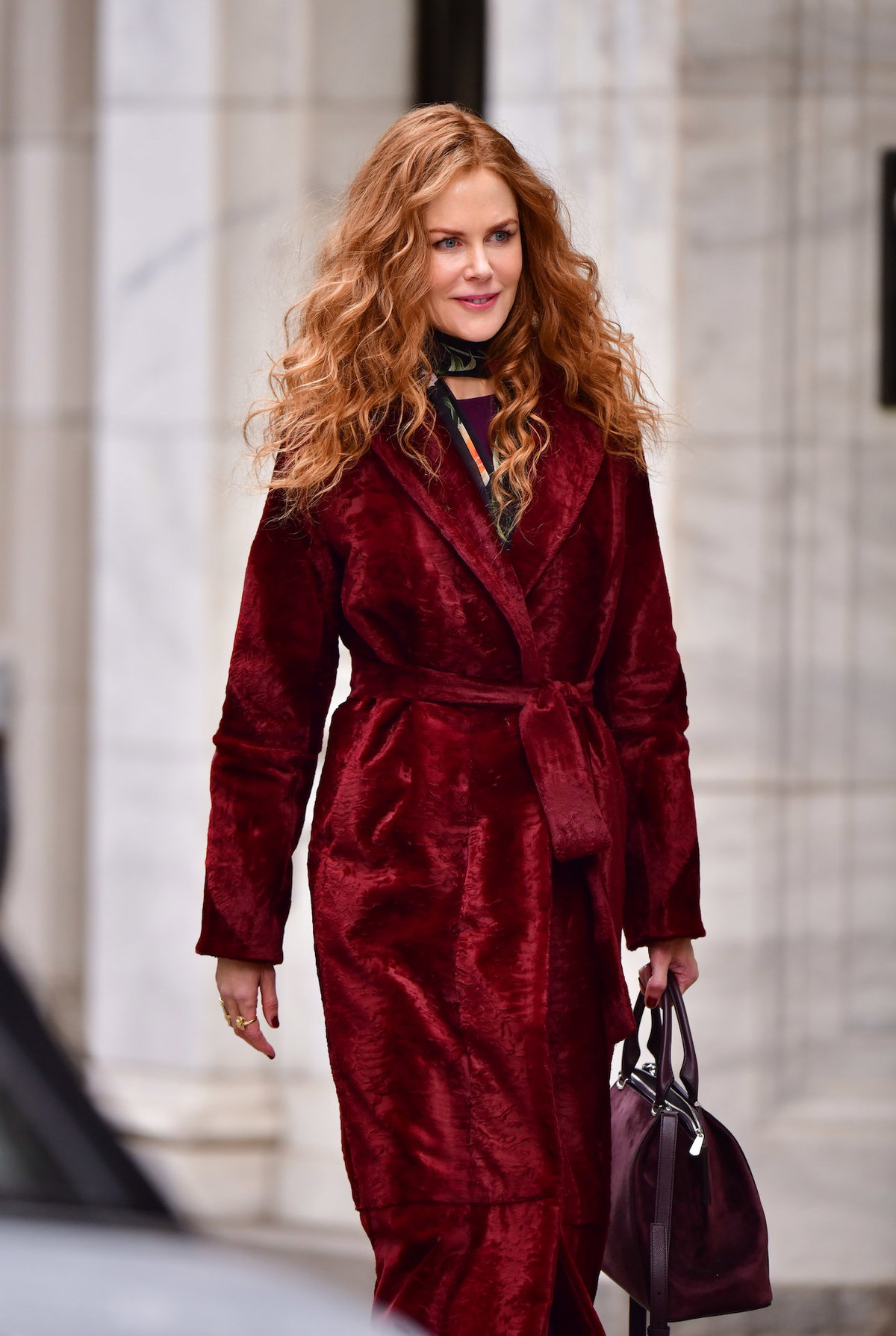 Nicole Kidman mit einem roten Mantel und offenen Locken auf der Straße.