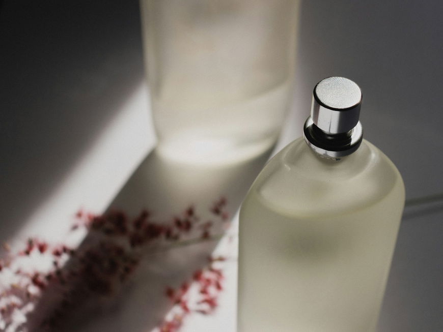 Parfum-Flakon mit rötlichen Trockenblumen im Hintergrund.