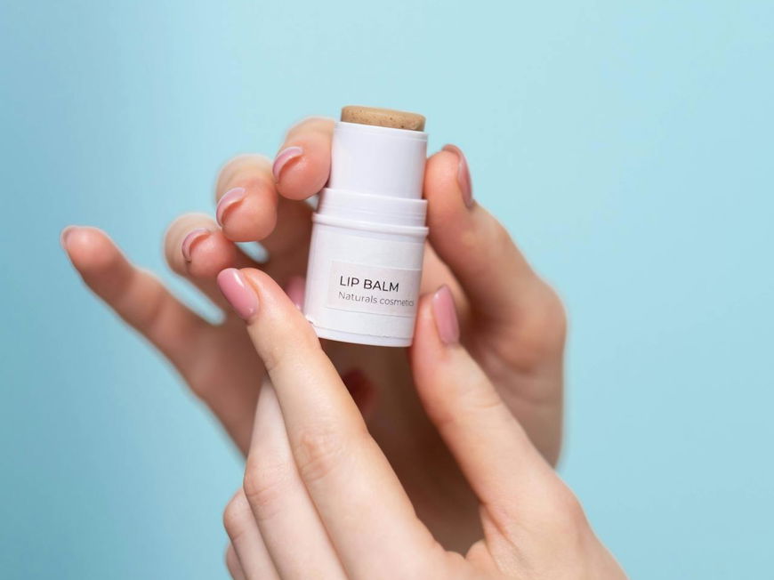 Ein Lip Balm wird in der Hand vor einem hellblauen Hintergrund gehalten.