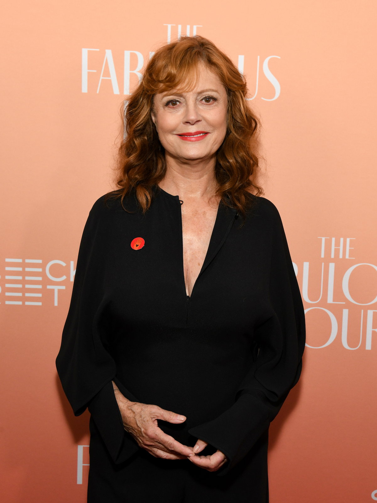 Susan Sarandon mit einem schwarzen Kleid vor einer aprikotfarbenen Wand.