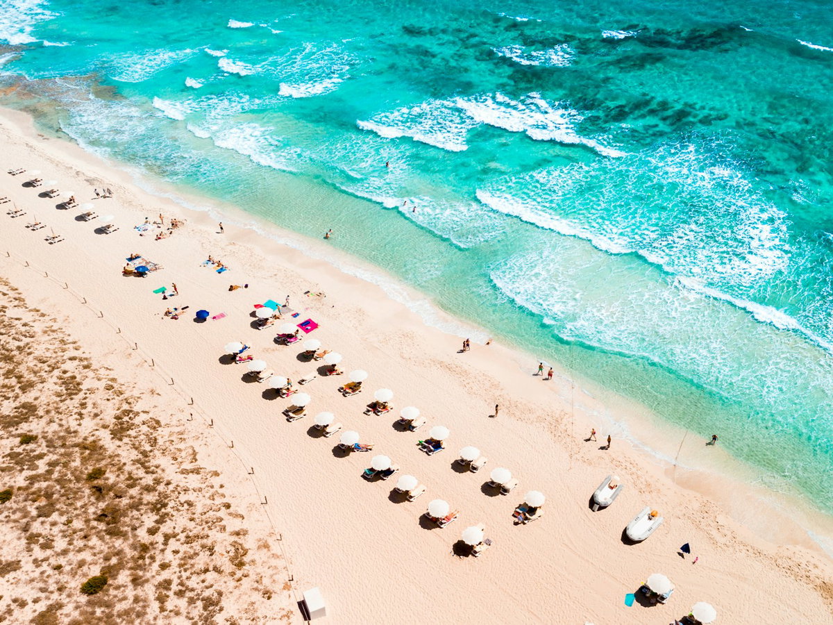 Der Strand von Formentera mit Liegen, Sonnenschirmen und Menschen.