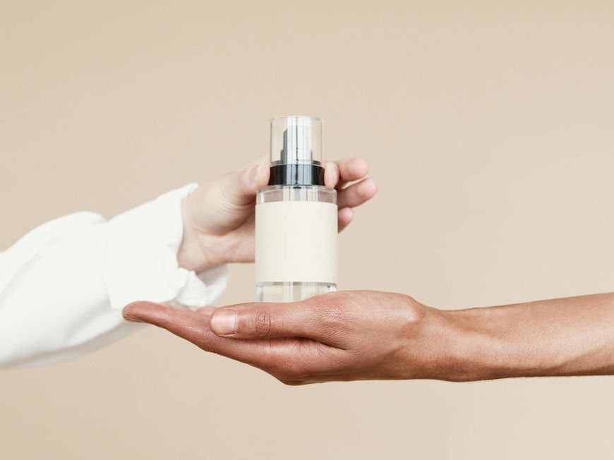 Eine Hand stellt ein Parfum in eine andere Hand.