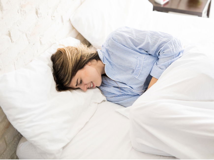 Eine Frau liegt mit Bauchschmerzen im Bett